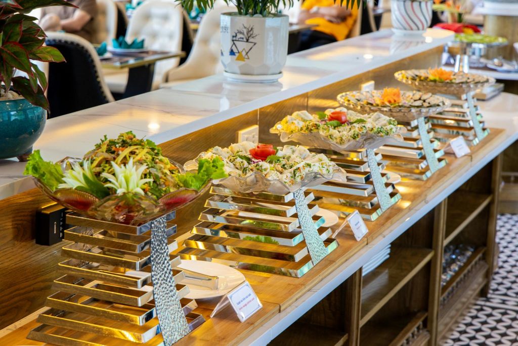 현대적이고 조명이 밝은 식사 공간을 배경으로 금속 가판대에서 다양한 요리를 즐길 수 있는 뷔페 디스플레이가 마련되어 있습니다.