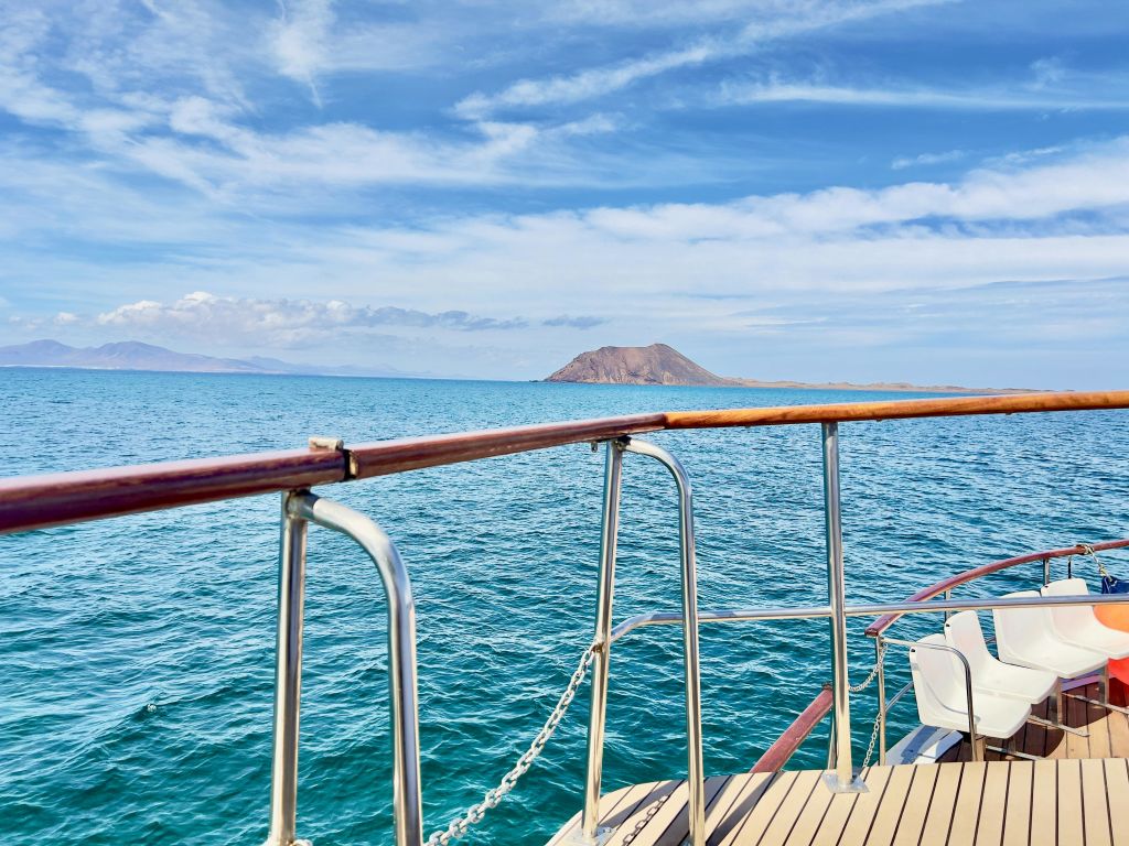 잔잔한 푸른 바다와 부분적으로 흐린 하늘 아래 먼 섬이 내려다보이는 난간이 있는 보트 데크.