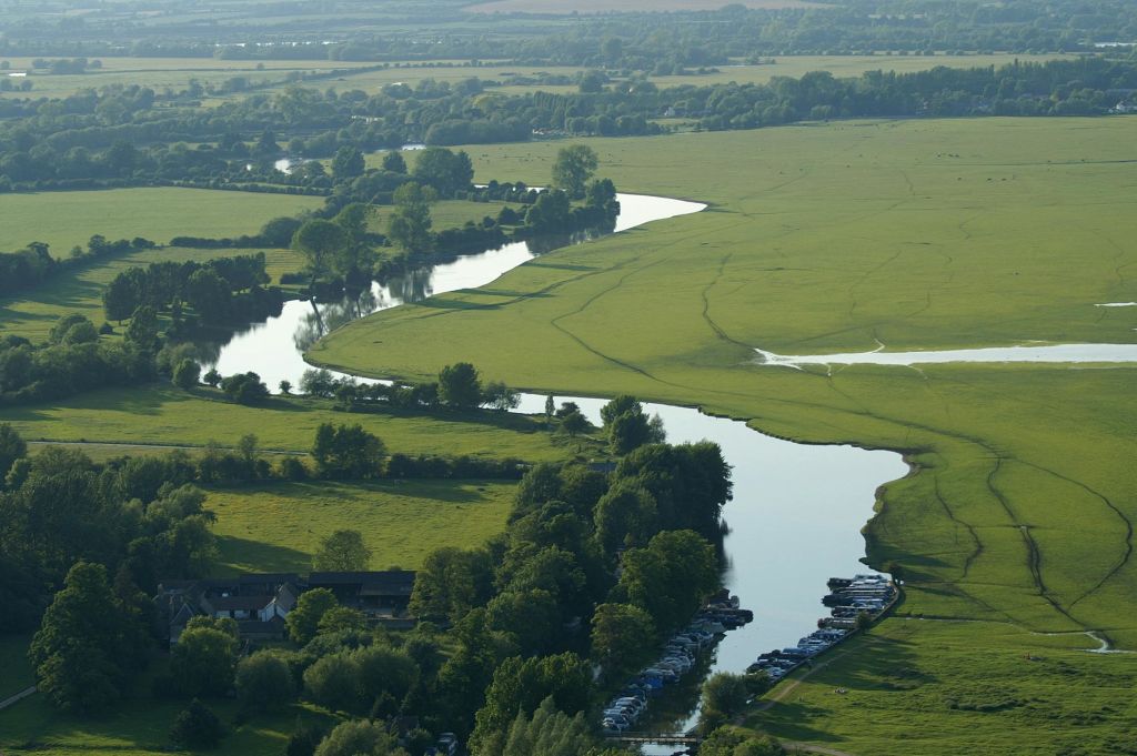 강둑을 따라 나무와 주차된 보트가 있는 푸른 들판을 통해 구불구불한 강을 볼 수 있습니다.