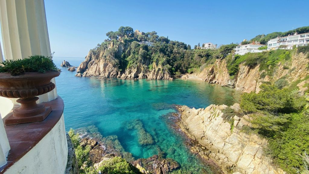 맑고 푸른 물, 험준한 절벽, 맑고 푸른 하늘 아래 나무 사이에 자리 잡은 건물이 있는 바위 해안선.