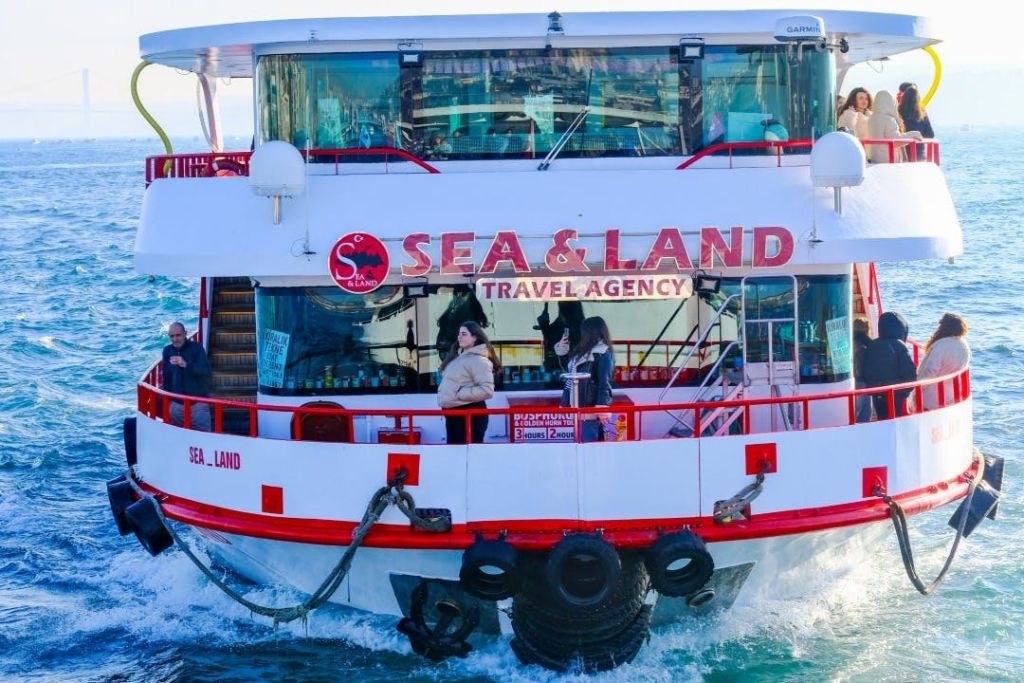 물 위에 'Sea & Land Travel Agency' 표지판이 있는 페리로 갑판의 승객들이 전망을 즐기고 있습니다.