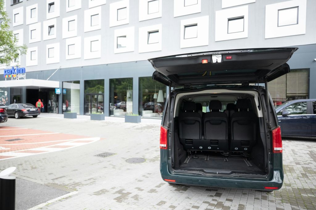 여러 개의 정사각형 창문이 있는 현대적인 호텔 건물 외부에 주차된 어두운 색의 밴 트렁크.