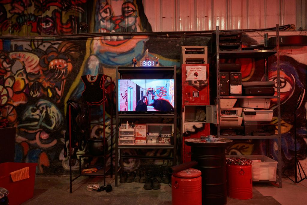 벽에 활기찬 낙서, 금속 선반 고정 장비, 장면이 표시된 TV, 보관함 및 다양한 물품이 있는 객실입니다.