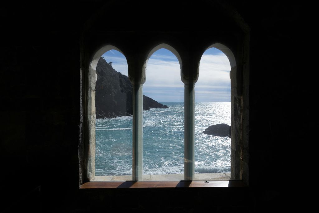 돌담에 세 개의 아치형 창문을 통해 바다와 절벽을 조망할 수 있으며, 햇빛이 물에 반사됩니다.