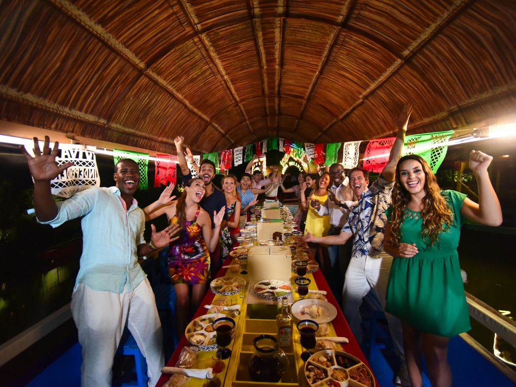 초가 지붕 아래에서 축제 분위기를 배경으로 음식과 음료를 즐기며 장식된 보트를 타고 축하하는 사람들의 모임입니다.