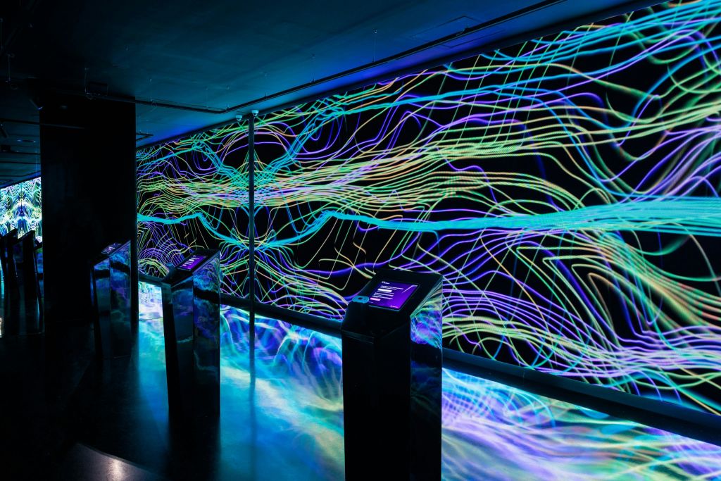 벽에 화려하고 흐르는 네온 같은 선이 있는 전시물입니다. 대화형 스크린은 전면의 스탠드에 있습니다.
