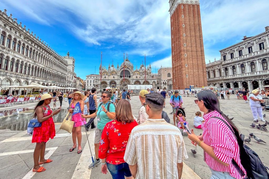 높은 종탑과 화려한 외관 등 청명한 하늘 아래 역사적 건물 근처에 사람들이 모여 있는 활기찬 광장.