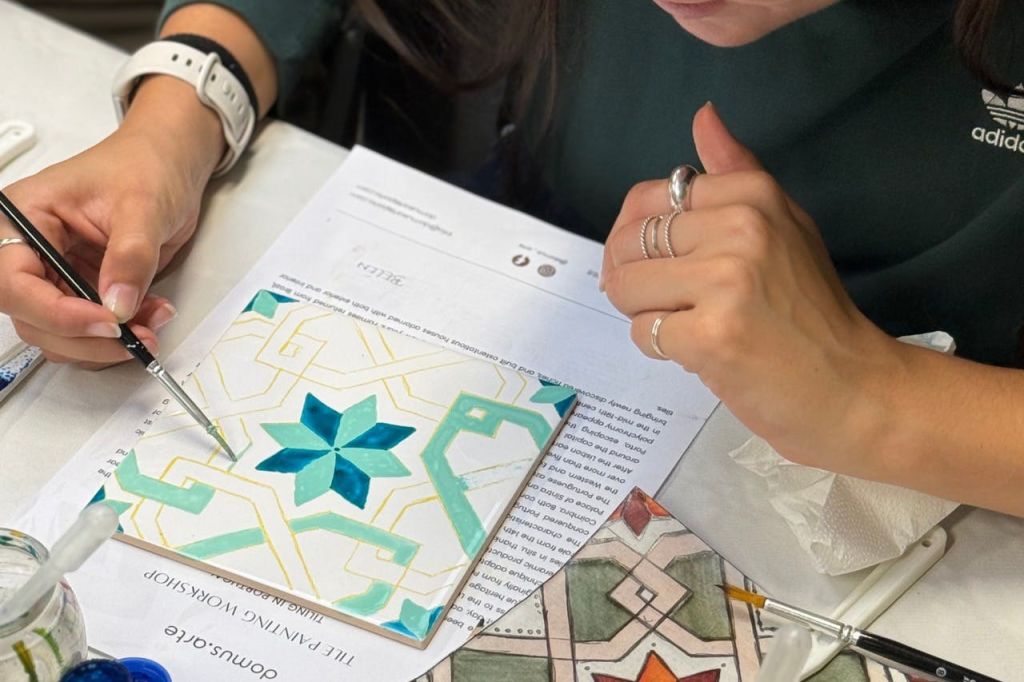 타일 위에 기하학적 디자인을 그리는 사람으로, 테이블 위에 종이와 기타 도구가 놓여 있습니다.