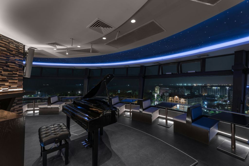 검은색 그랜드 피아노, 좌석 공간, 커다란 창문이 있는 현대적인 객실로 도시 풍경의 야경을 감상할 수 있습니다.