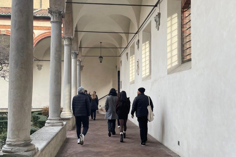 기둥과 높은 천장이 있는 아치형 복도를 걷는 사람들은 겨울 옷을 입고 있습니다.