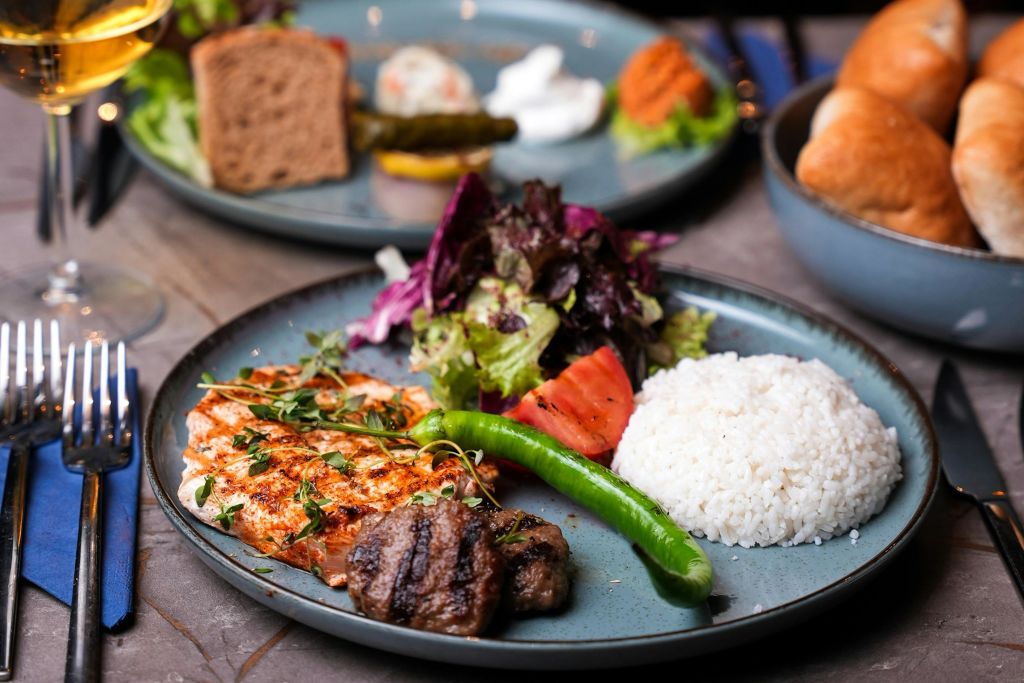 구운 닭고기, 쇠고기 패티, 밥, 샐러드, 토마토, 청양고추가 담긴 접시. 다양한 애피타이저를 배경으로 한 또 다른 접시.