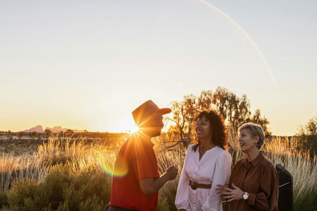 해 질 녘 들판에 세 사람이 서서 웃고 있습니다. 키 큰 풀과 나무를 배경으로 말이죠.