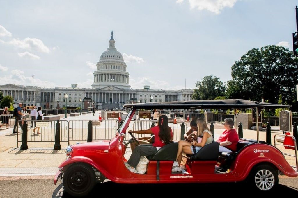 맑은 날 미국 국회의사당 건물 근처에 주차된 승객이 탄 빨간 골프 카트.