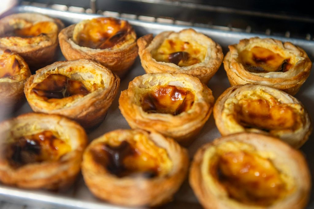 갓 구운 커스터드 타르트와 황금색의 각질이 돋보이는 크러스트, 캐러멜 처리된 상판이 담긴 트레이입니다.