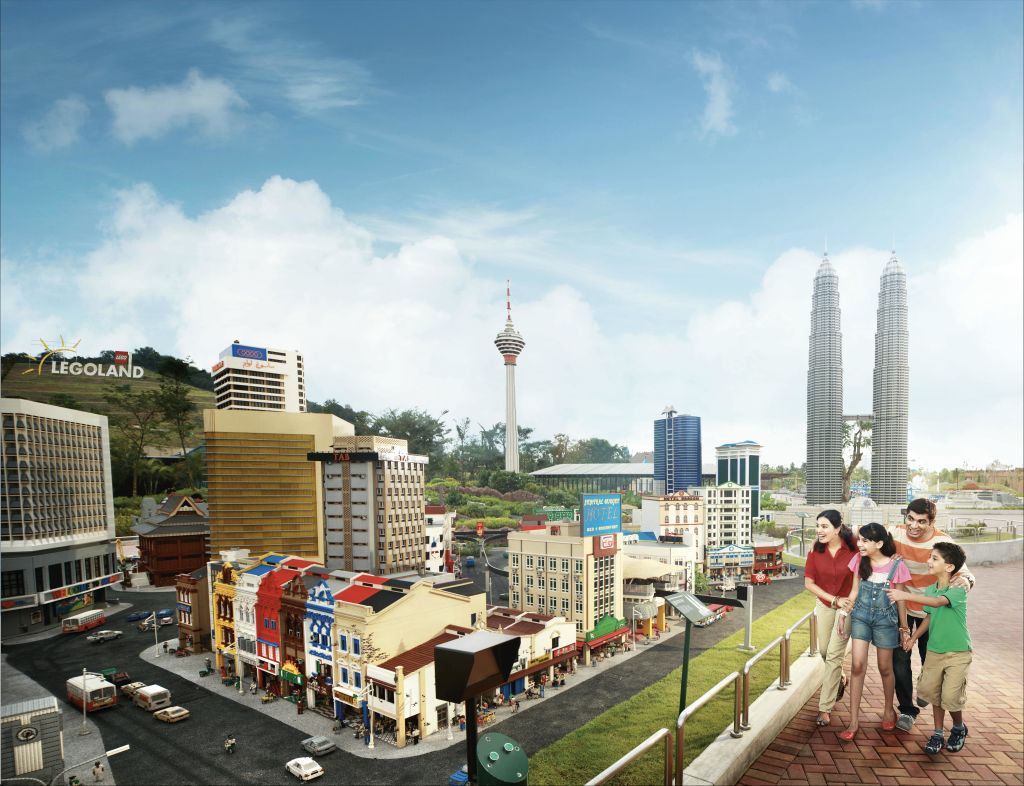 밝고 푸른 하늘 아래 디테일한 건물과 상징적인 탑이 있는 4인 가족이 미니어처 도시 풍경을 감상합니다.