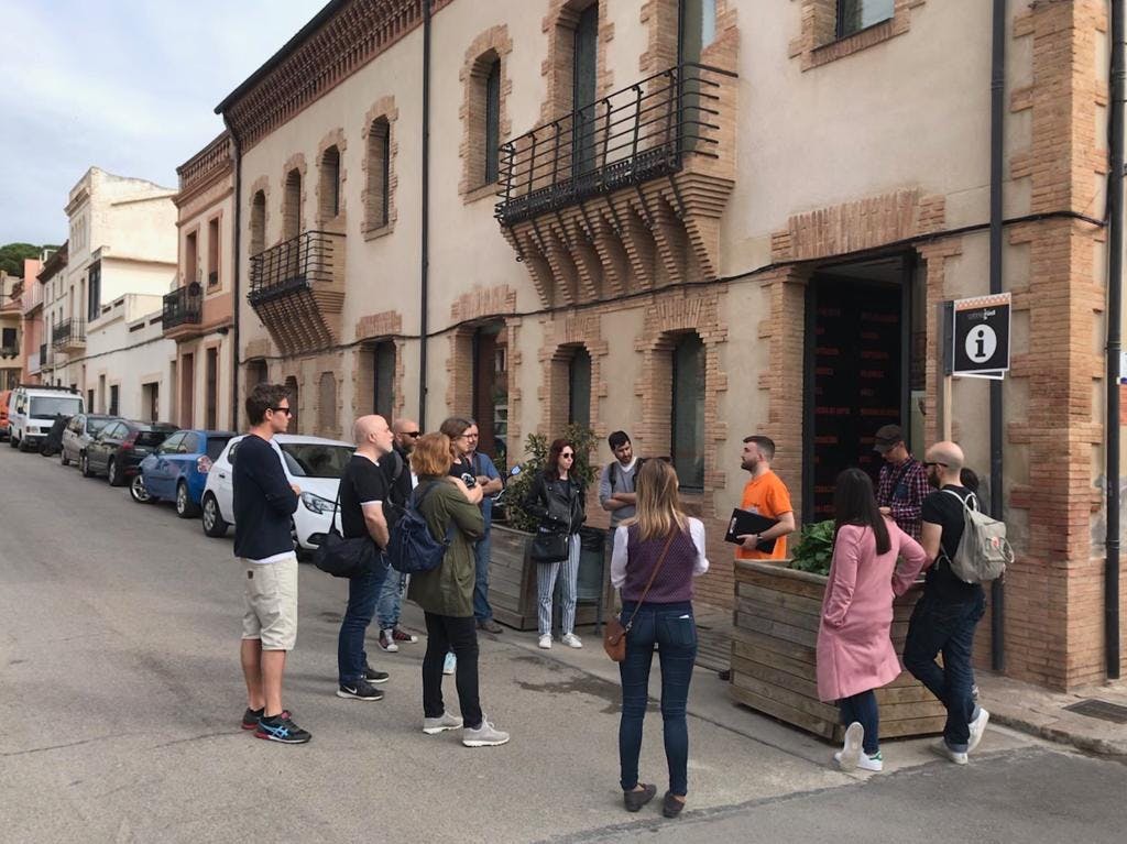 한 무리의 사람들이 아치형 창문과 발코니가 있는 건물 앞 거리에 서서 대화를 나누고 있습니다.