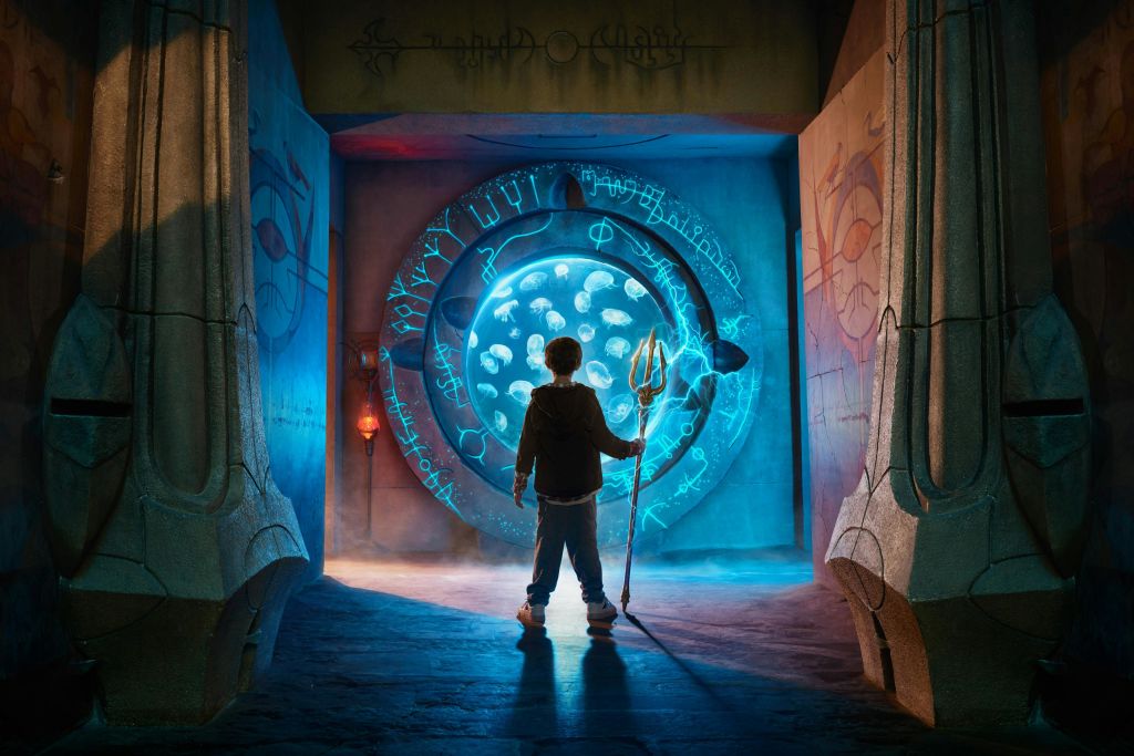 삼지창을 들고 있는 한 사람이 고대 석재로 둘러싸인 상징물이 있는 빛나는 원형 포털 앞에 서 있습니다.