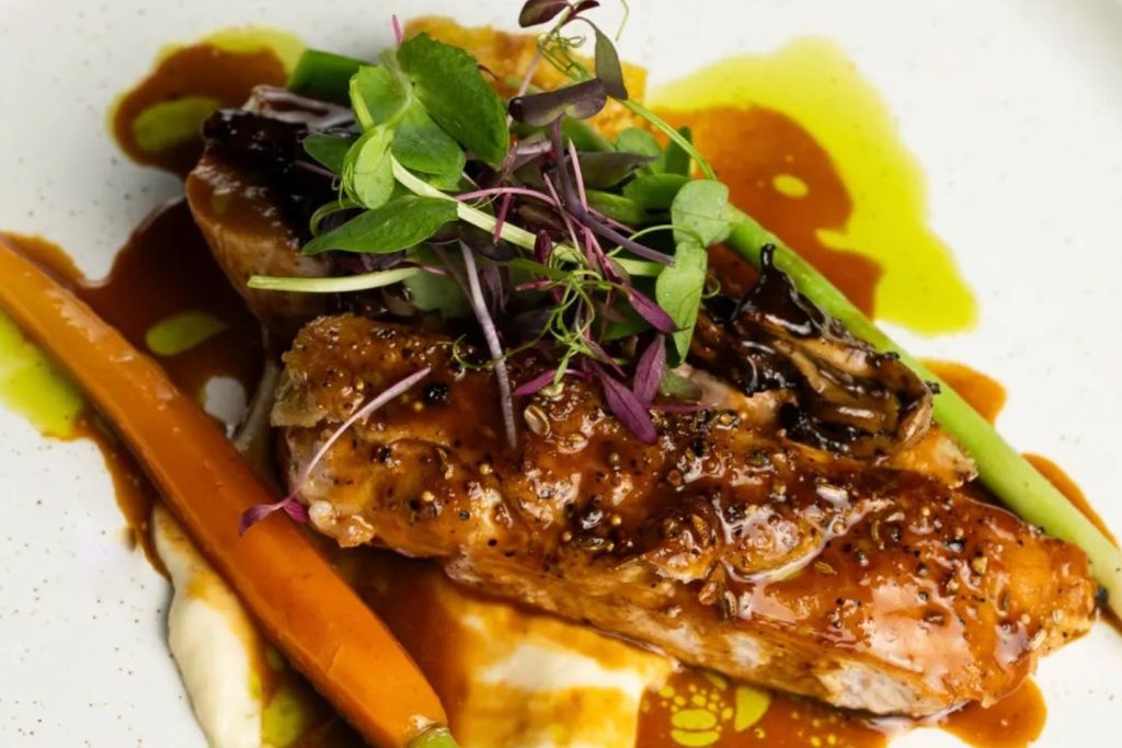 유리 고기, 당근, 신선한 마이크로그린을 접시에 담아 소스와 퓨레 위에 올린 고급 요리입니다.