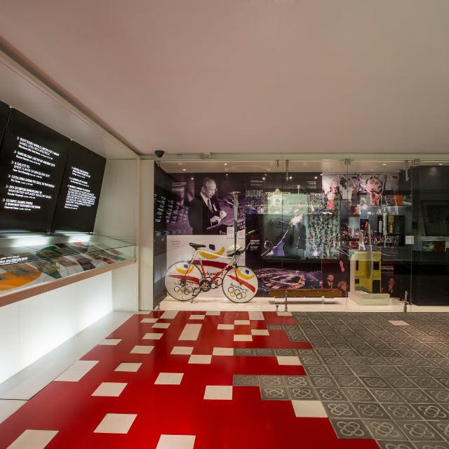 박물관 전시물에는 올림픽 역사에 대한 빨간색과 흰색 자전거, 벽 이미지, 전시 케이스 및 정보 패널이 전시되어 있습니다.