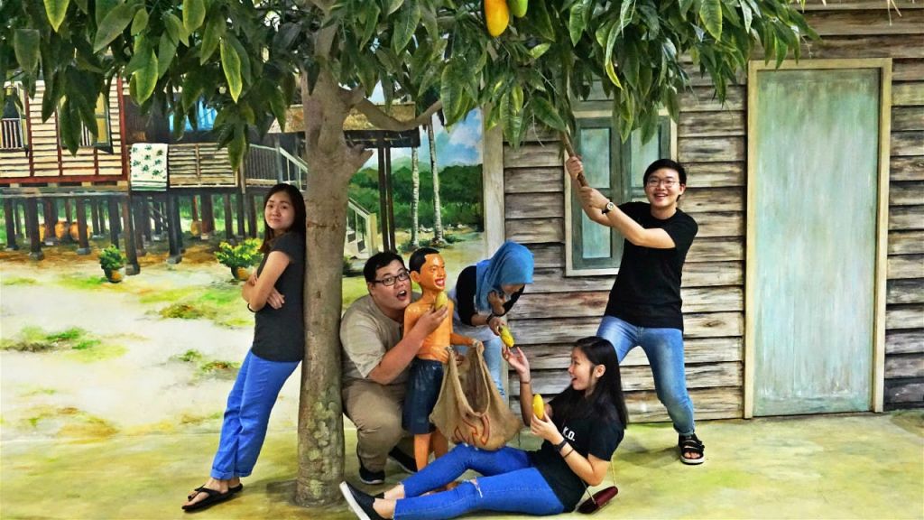 소박한 건물 근처의 망고 나무 주위에서 장난스럽게 포즈를 취하는 다섯 명, 일부는 망고를 잡고 손을 뻗습니다.