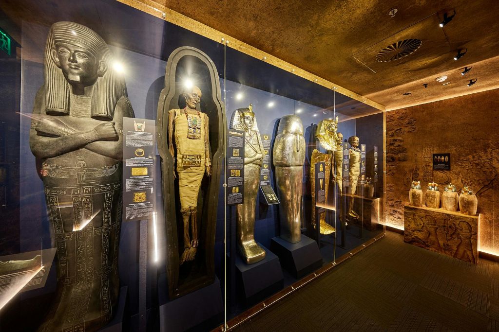 박물관 전시물에 이집트 석관과 미라가 전시되어 있으며, 각 유물을 설명하는 정보용 명판이 있습니다.