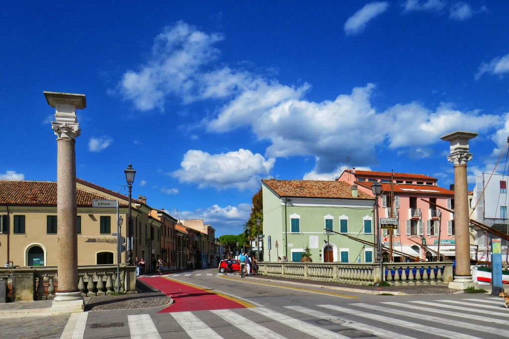 화려한 건물, 도로의 교차선, 빈티지한 빨간 차, 사람들, 구름이 있는 푸른 하늘이 있는 햇살 가득한 거리 풍경.