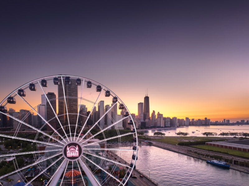 높은 도시 건물과 석양의 하늘을 배경으로 물가 근처의 대관람차.