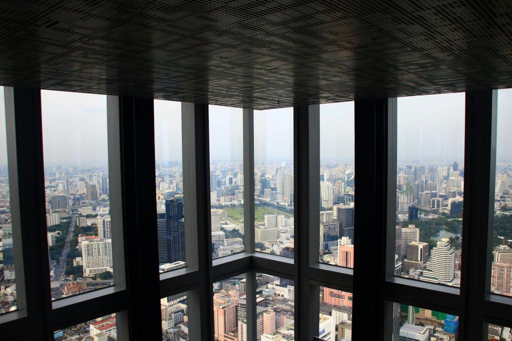 커다란 창문 모퉁이에서 바라보는 도시 풍경의 고층 전망은 흐린 하늘 아래 수많은 고층 건물과 건물을 보여줍니다.