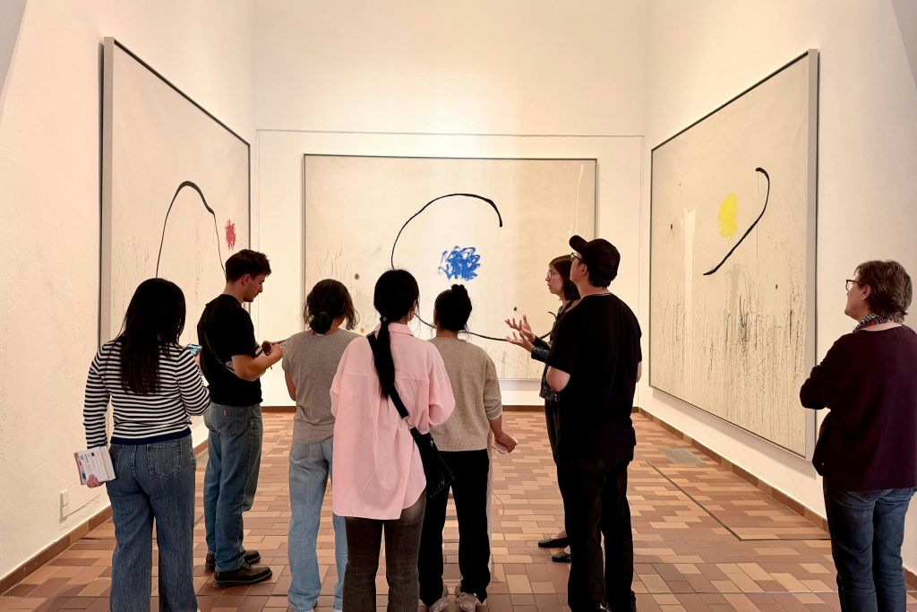 타일 바닥과 흰색 벽이 있는 아트 갤러리에서 추상화를 감상하는 한 무리의 사람들.