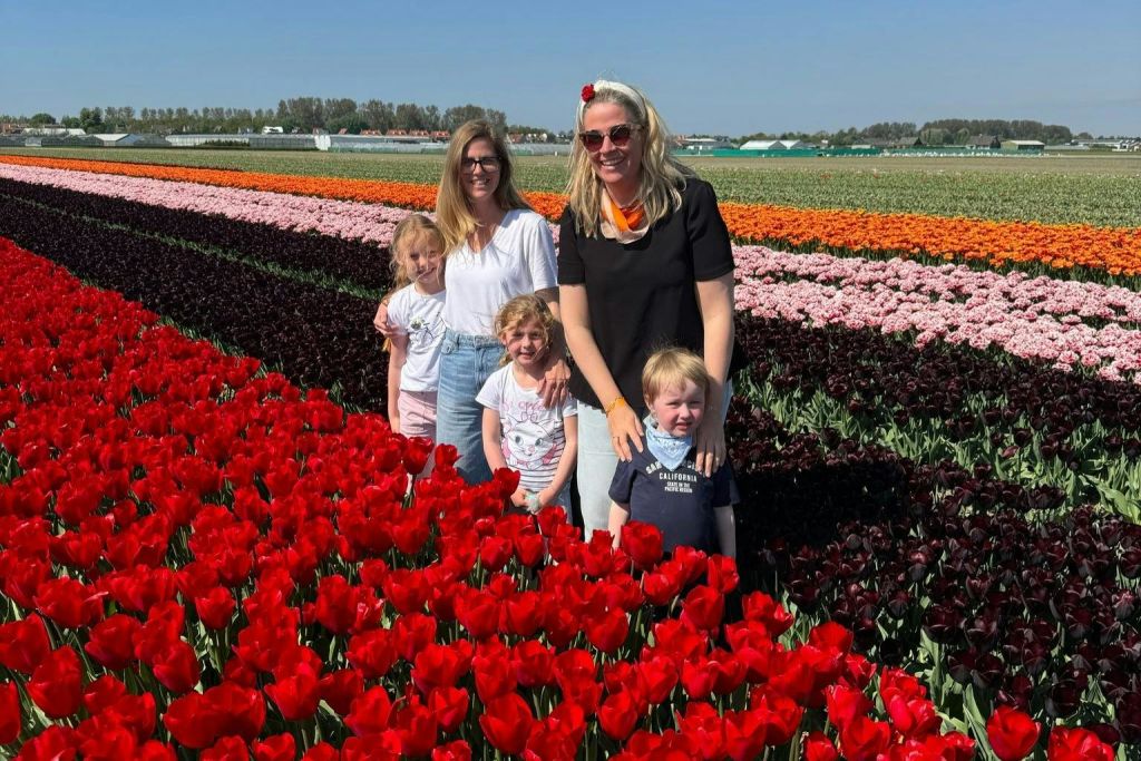 맑고 푸른 하늘 아래 들판에서 활기찬 줄무늬 튤립 앞에서 포즈를 취하고 있는 두 여자와 세 아이.