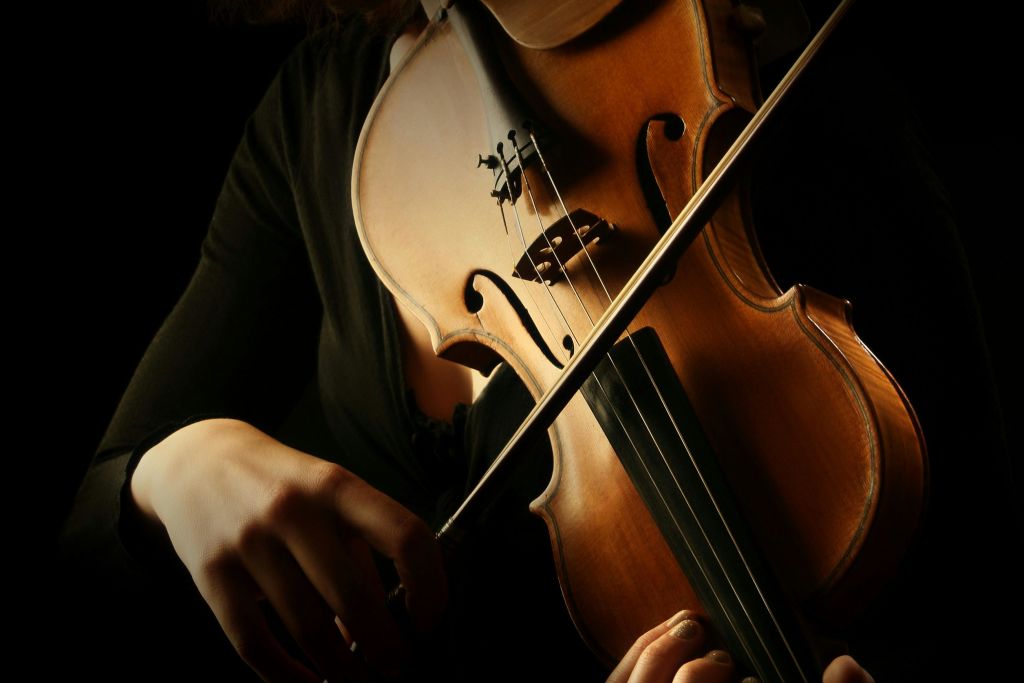 바이올린을 연주하는 사람의 클로즈업으로 따뜻한 조명 아래에서 악기와 움직이는 활을 강조합니다.