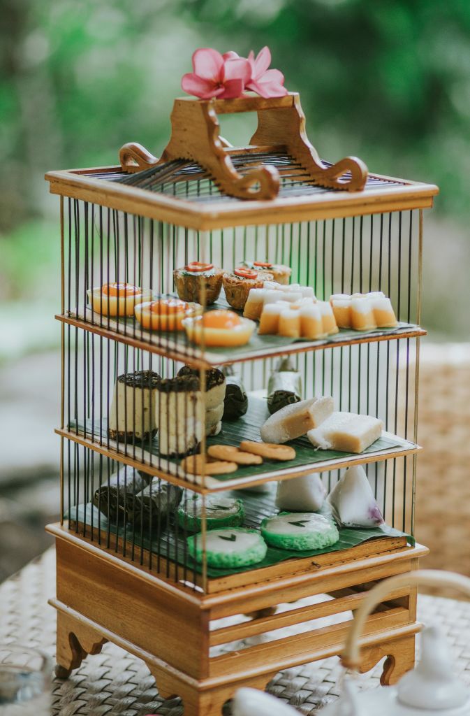 다채로운 페이스트리와 간식을 다양하게 담을 수 있는 3단 나무 거치대는 녹음이 흐릿한 야외를 배경으로 합니다.