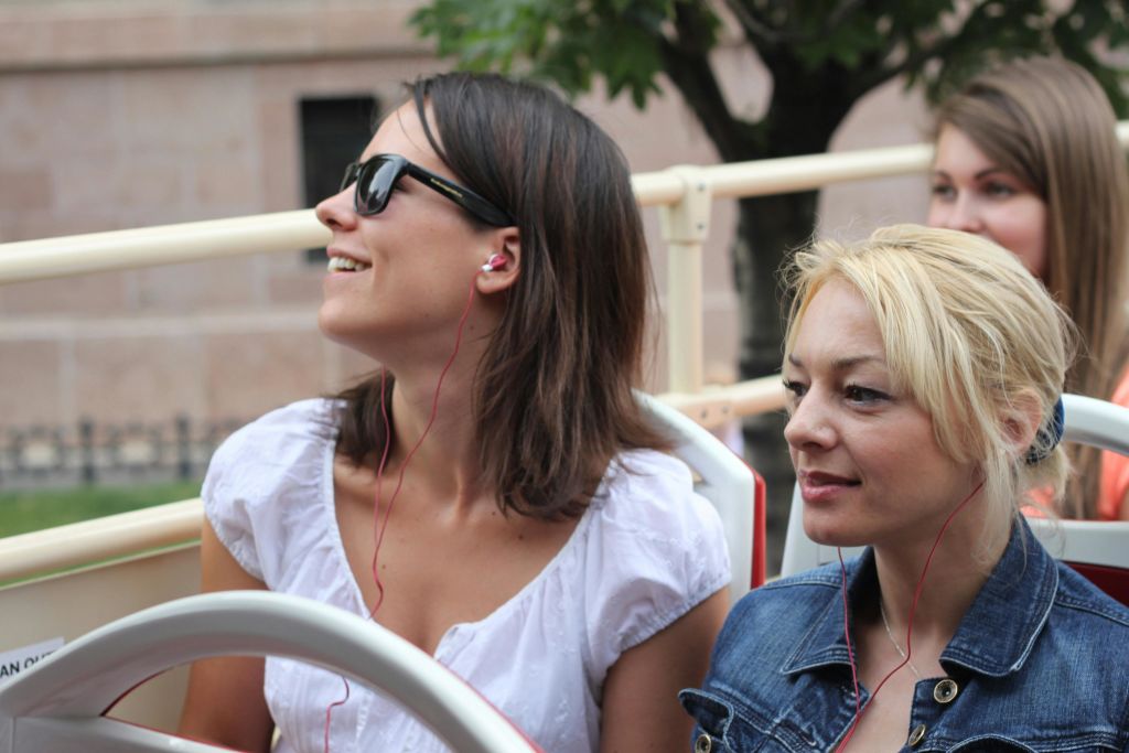 이어폰을 끼고 야외 버스에 앉아 있는 두 명의 여성이 나무와 건물을 배경으로 사진을 찍고 있습니다.