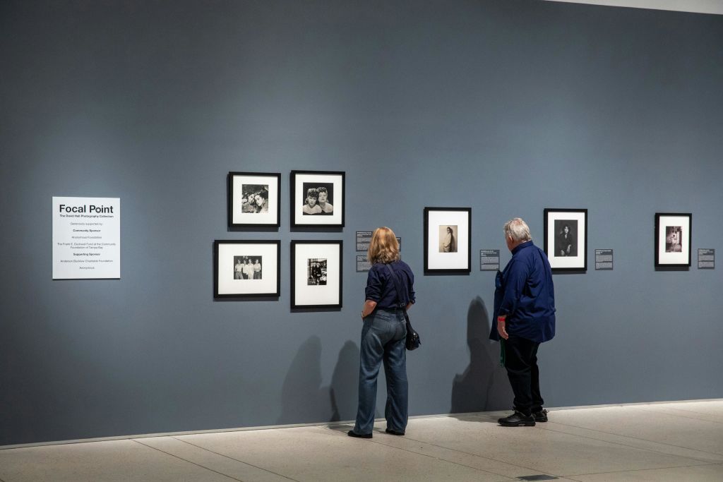 두 사람이 아트 갤러리의 푸른 벽에 걸린 흑백 액자 사진을 보고 있습니다.