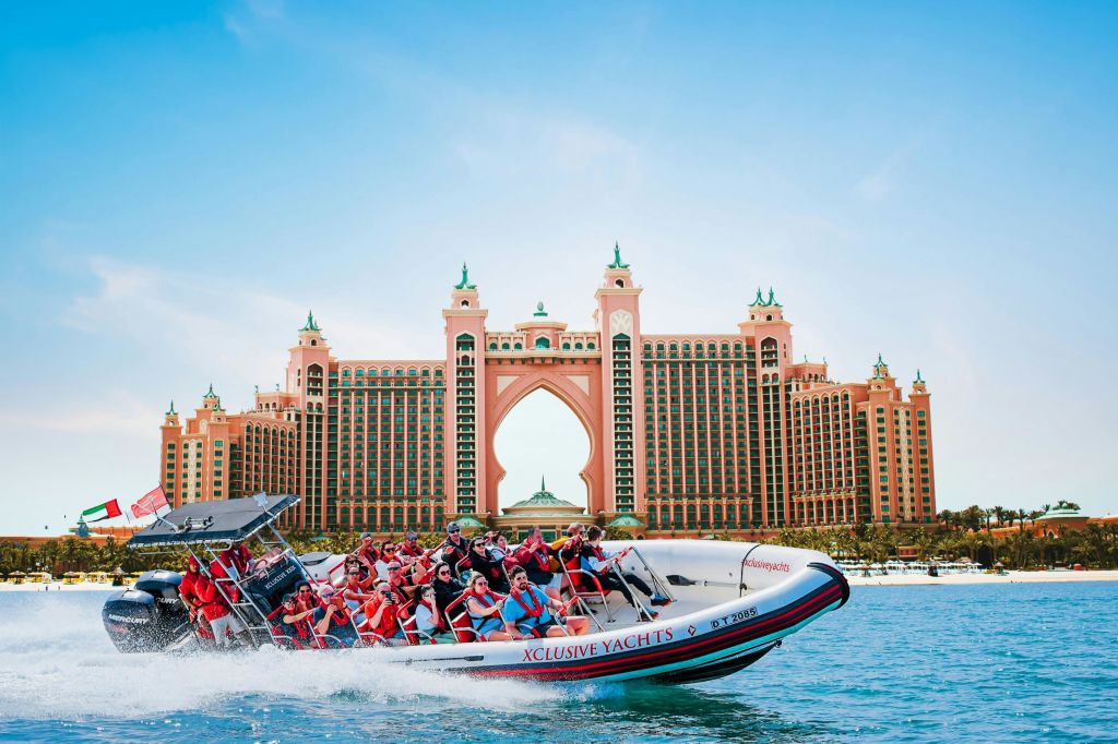 맑고 푸른 하늘 아래 크고 분홍색 아치 모양의 고급 호텔 앞에서 쾌속정을 타는 사람들.