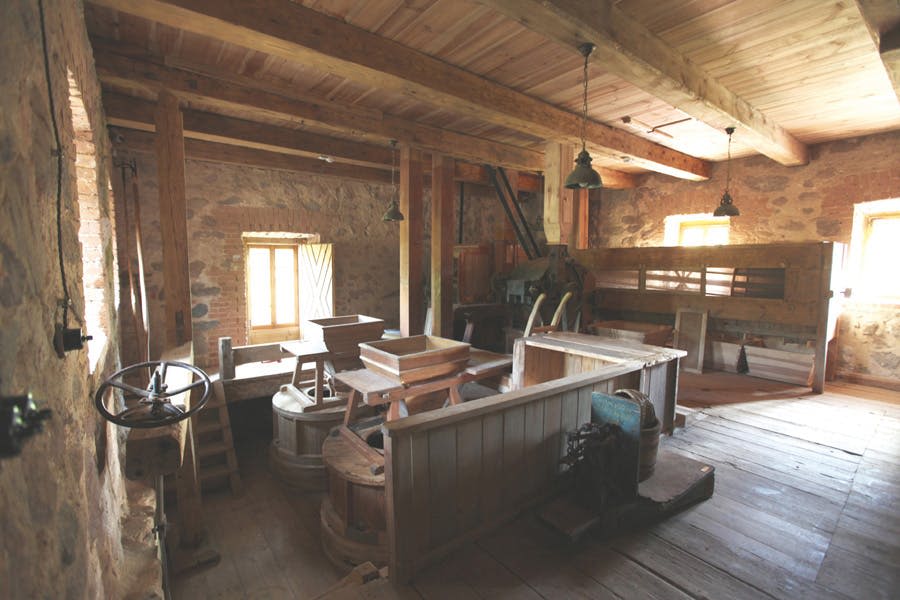 창문을 통해 흐르는 나무 들보, 다양한 밀링 장비, 햇빛이 있는 오래된 방앗간 내부.
