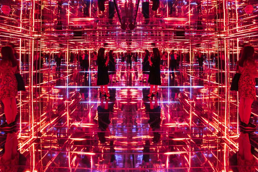 거울과 네온 불빛이 가득한 방에 한 사람이 서서 활기차고 반사되는 환경을 조성합니다.