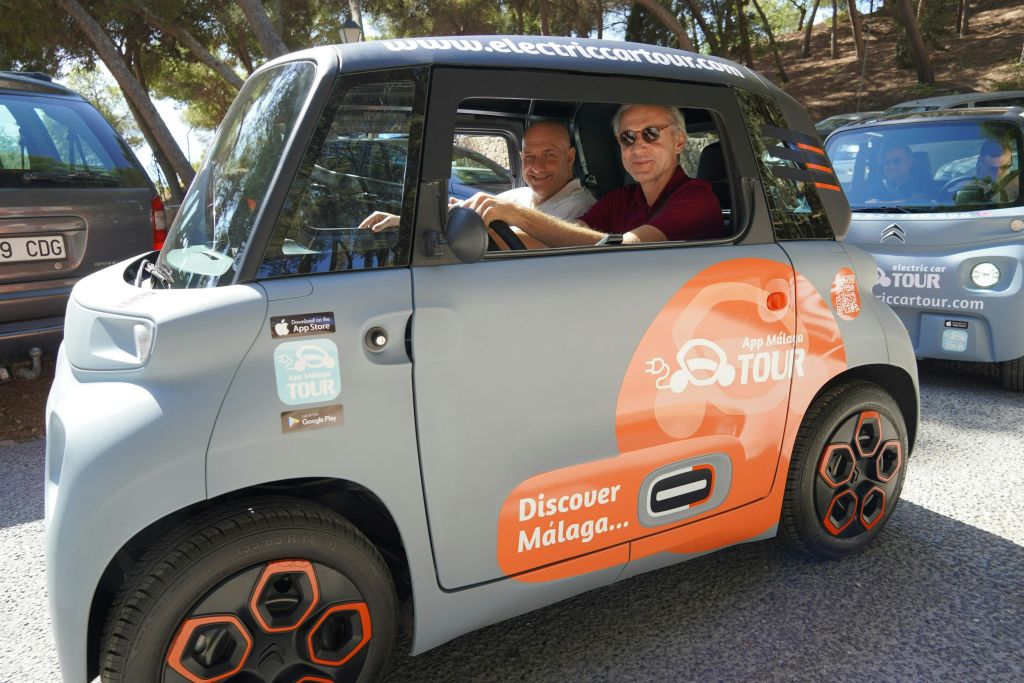 "Discover Málaga" 와 "App Málaga Tour" 데칼을 들고 작은 전기차에 앉아 미소를 짓고 있는 두 남성.