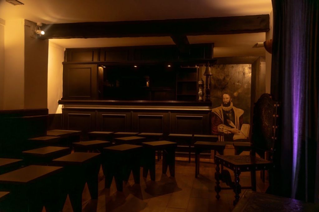 어두운 나무 바, 의자, 역사적인 인물의 대형 초상화가 있는 조명이 희미한 객실입니다. 보라색 조명으로 부분적으로 그려진 커튼.