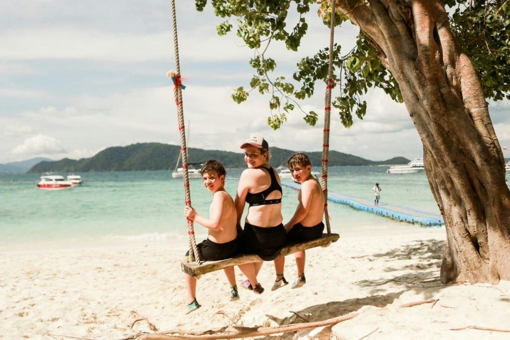 아름다운 바다와 산을 배경으로 모래 해변에서 밧줄을 타고 그네를 타는 세 사람.