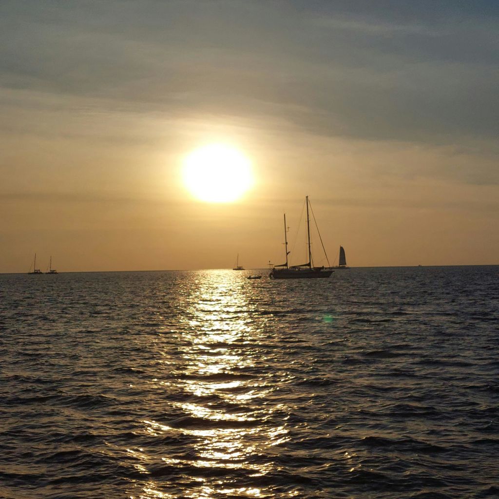 석양에 고요한 바다에서 즐기는 요트와 햇살이 물 위에서 금빛 빛을 반사합니다.