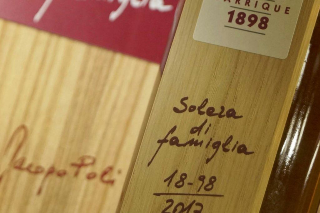 "Solera di famiglia 1898-2013" 이라는 필기 텍스트와 상단에 "1898" 이 있는 빨간색 라벨이 있는 목재 표면 클로즈업.