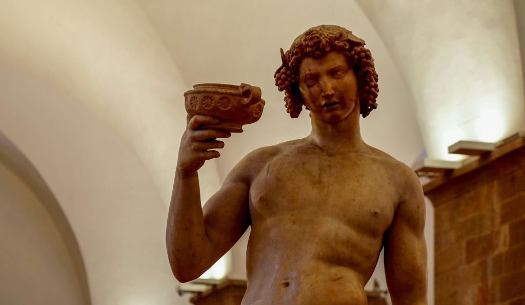 실내 박물관 환경을 배경으로 장식용 컵을 들고 있는 곱슬머리 누드 피규어의 고전적인 조각상.