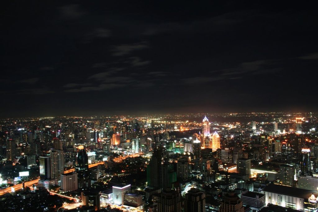 희미한 구름과 함께 어두운 하늘을 배경으로 밝게 빛나는 고층 건물과 건물이 있는 야간 도시 풍경.