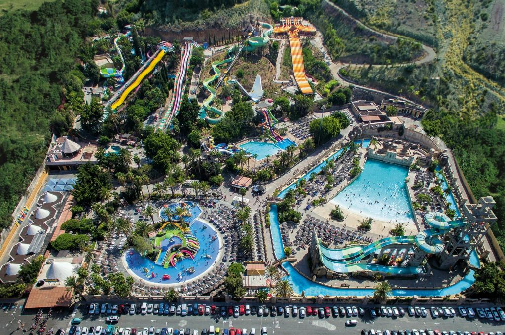 여러 개의 워터 슬라이드, 파도 수영장, 느긋한 강, 수많은 일광욕과 우산을 갖춘 대형 워터 파크의 공중 전망.