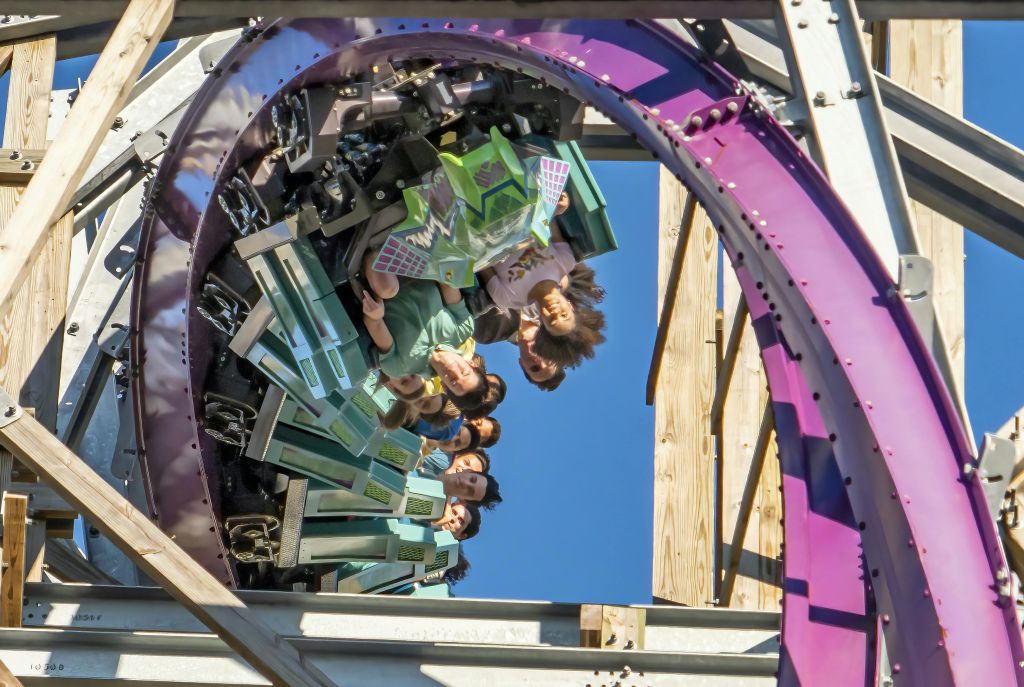 수직 루프에서 롤러코스터를 타는 승객은 맑고 푸른 하늘을 배경으로 거꾸로 달립니다.