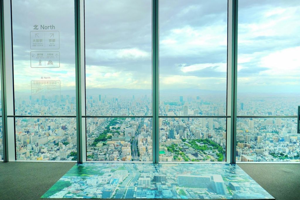 높은 건물의 커다란 창문에서 내려다보는 도시 풍경, 전경의 바닥에 파노라마 지도가 있습니다.