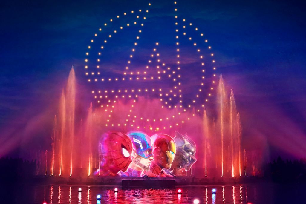 화려한 분수 위로 하늘에 빛나는 어벤져스 로고와 밤에는 슈퍼히어로의 얼굴을 볼 수 있습니다.