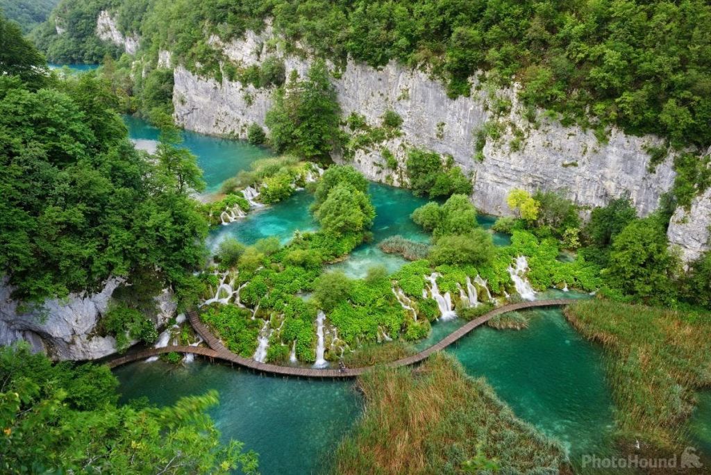 청록색 호수와 폭포, 녹음과 바위 절벽을 가로지르는 나무길이 있는 울창한 풍경.