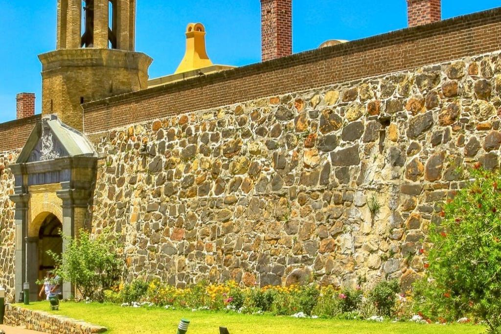 맑고 푸른 하늘 아래 굴뚝과 풀이 우거진 마당, 꽃이 피어 있는 돌과 벽돌 벽.